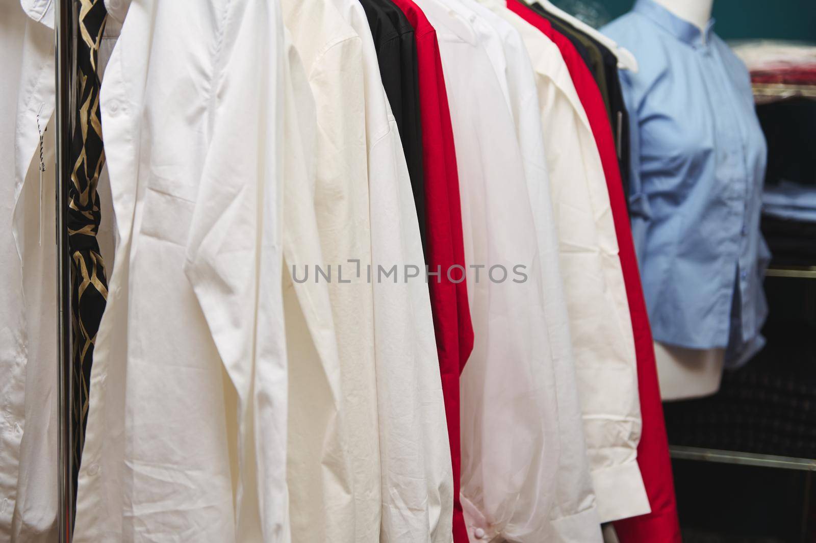 Details of women's clothes hanging on hangers in clothing design and tailoring atelier of fashion boutique. Cropped image of exclusive women's shirt on hangers