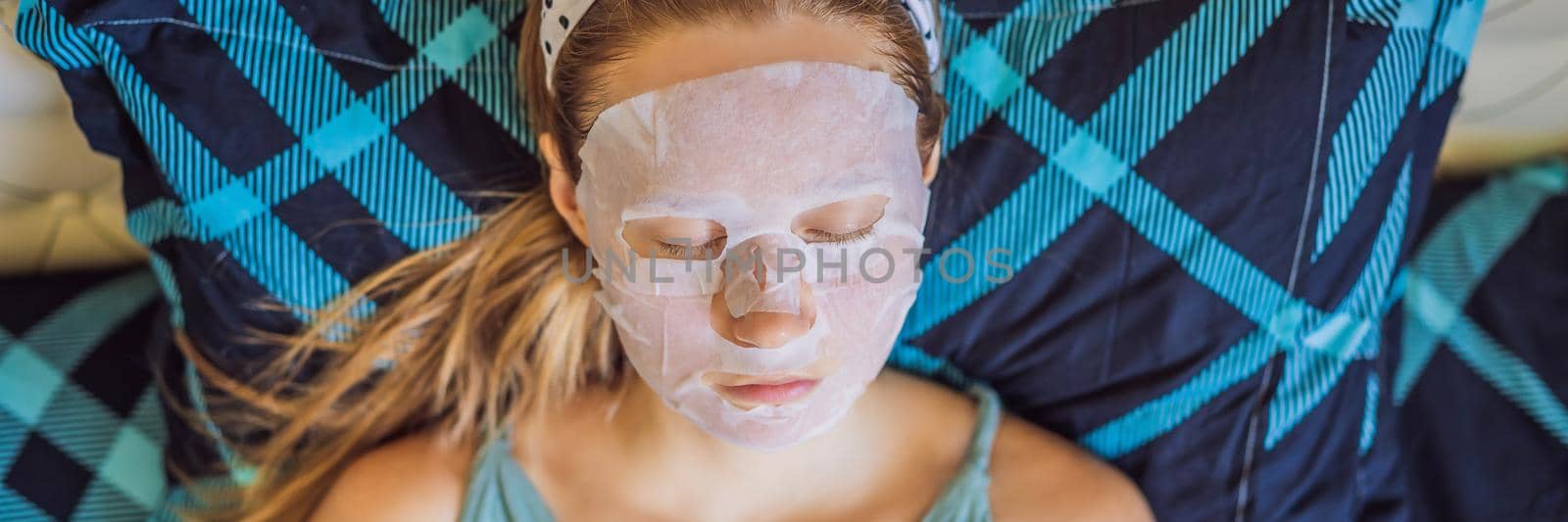 Young red-haired woman doing facial mask sheet. Beauty and Skin Care Concept. BANNER, LONG FORMAT