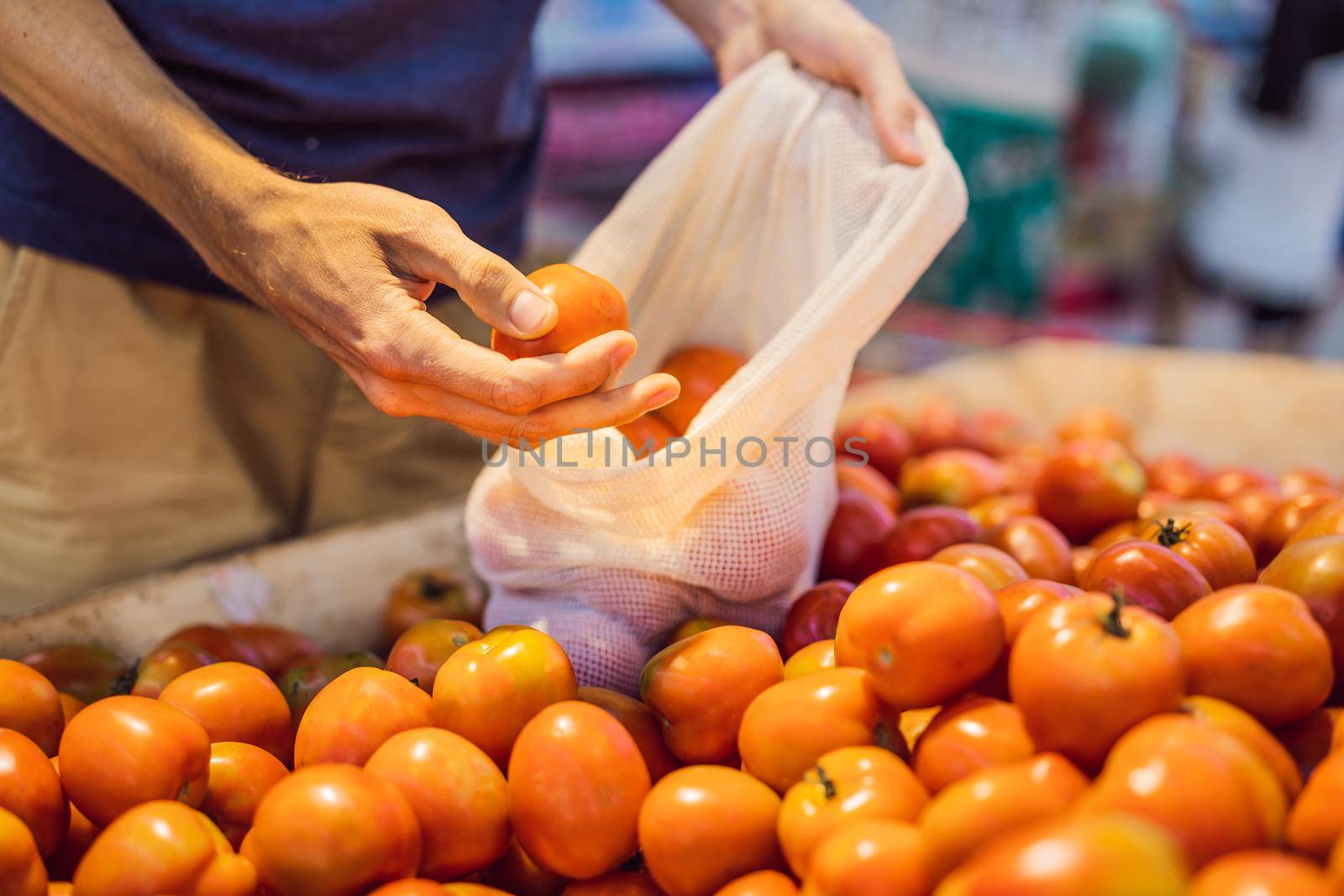 Man chooses tomatoes in a supermarket without using a plastic bag. Reusable bag for buying vegetables. Zero waste concept.