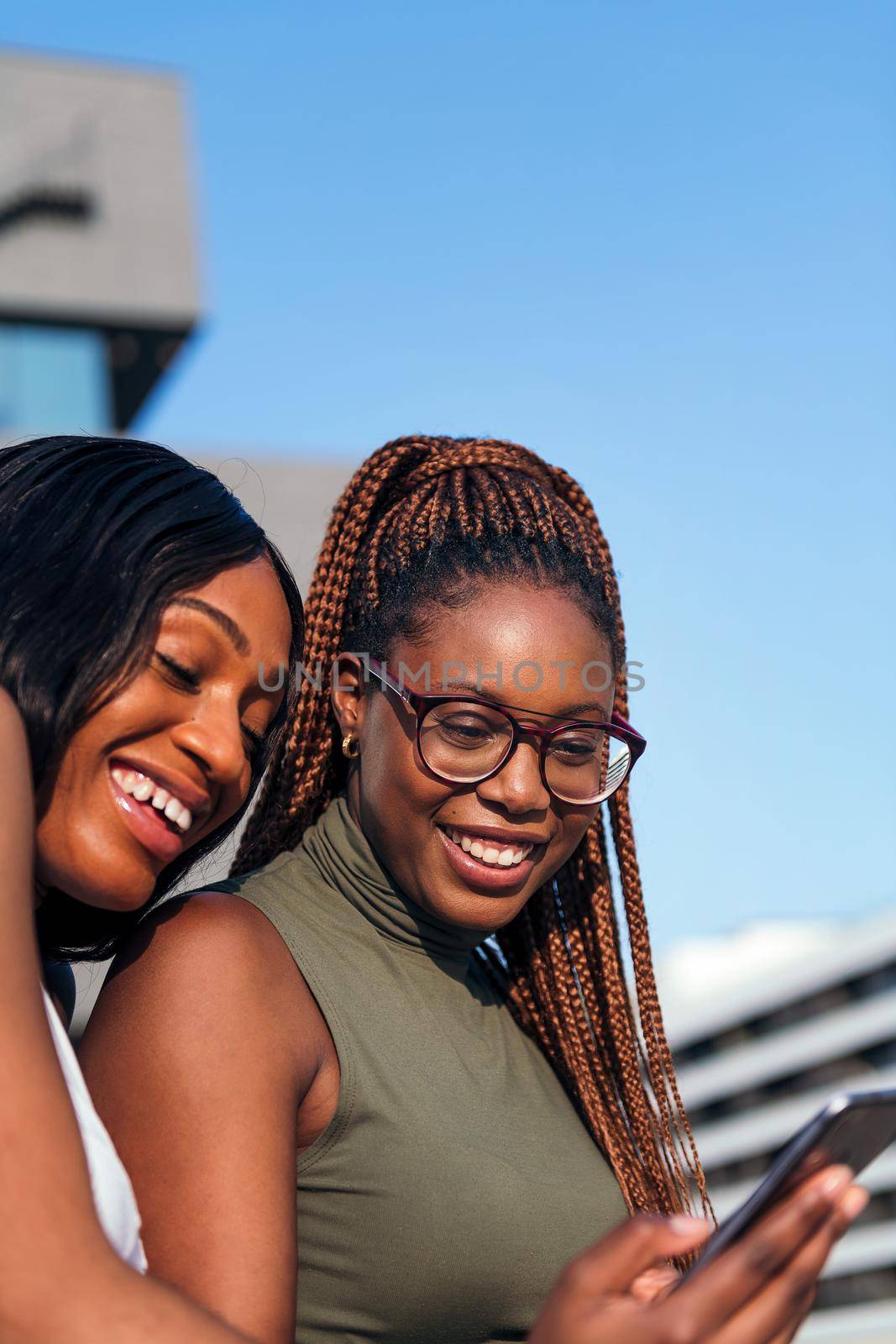 vertical photo of two young black women smiling and having fun looking at the cell phone, concept of youth and communication technology, copy space for text