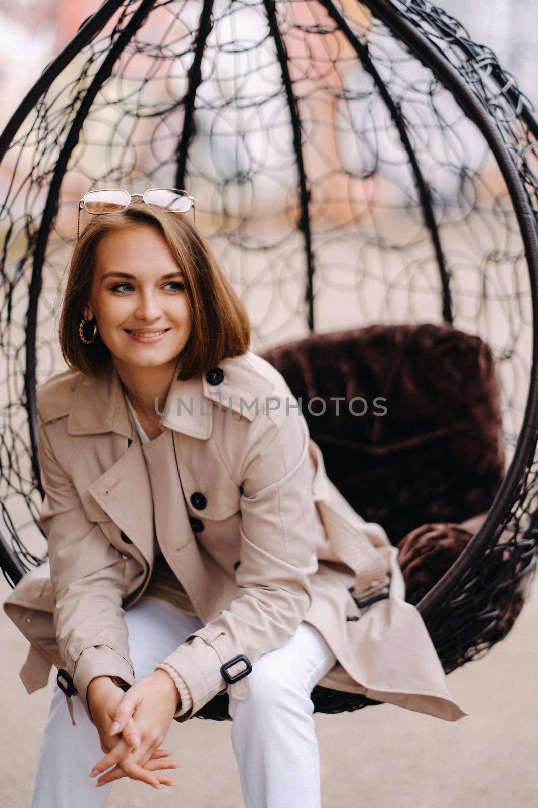 A happy stylish girl In a gray coat is sitting outside in an armchair.
