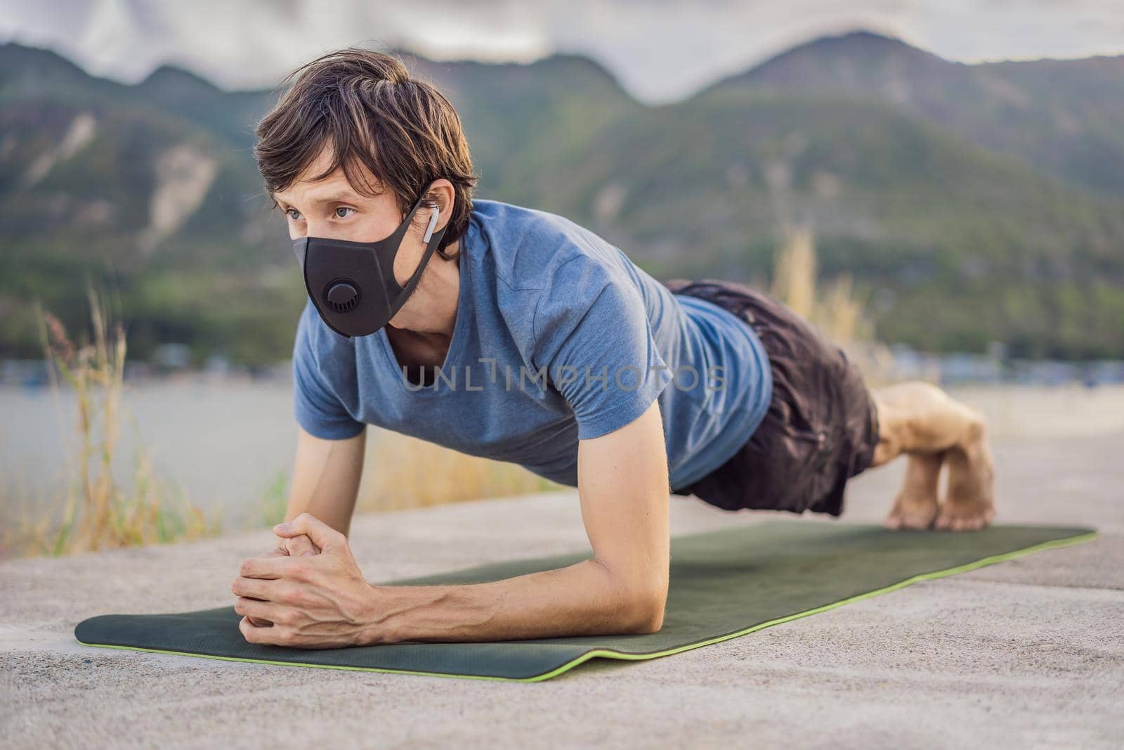 Young man in medical mask performing some workouts in the park during coronavirus quarantine, Coronavirus pandemic Covid-19. Sport, Active life in quarantine surgical sterilizing face mask protection. Outdoor run on athletics track in Corona Outbreak by galitskaya