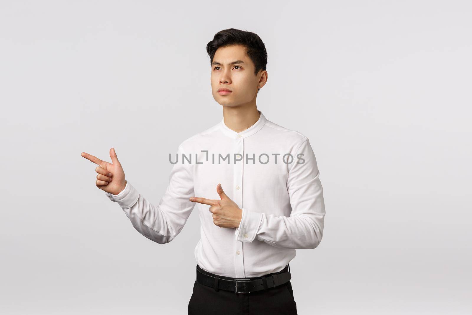 Serious-looking sulking thoughtful asian guy in formal outfit, look and pointing left thinking, pondering, making important decision, ready pick variant, standing pensive white background.