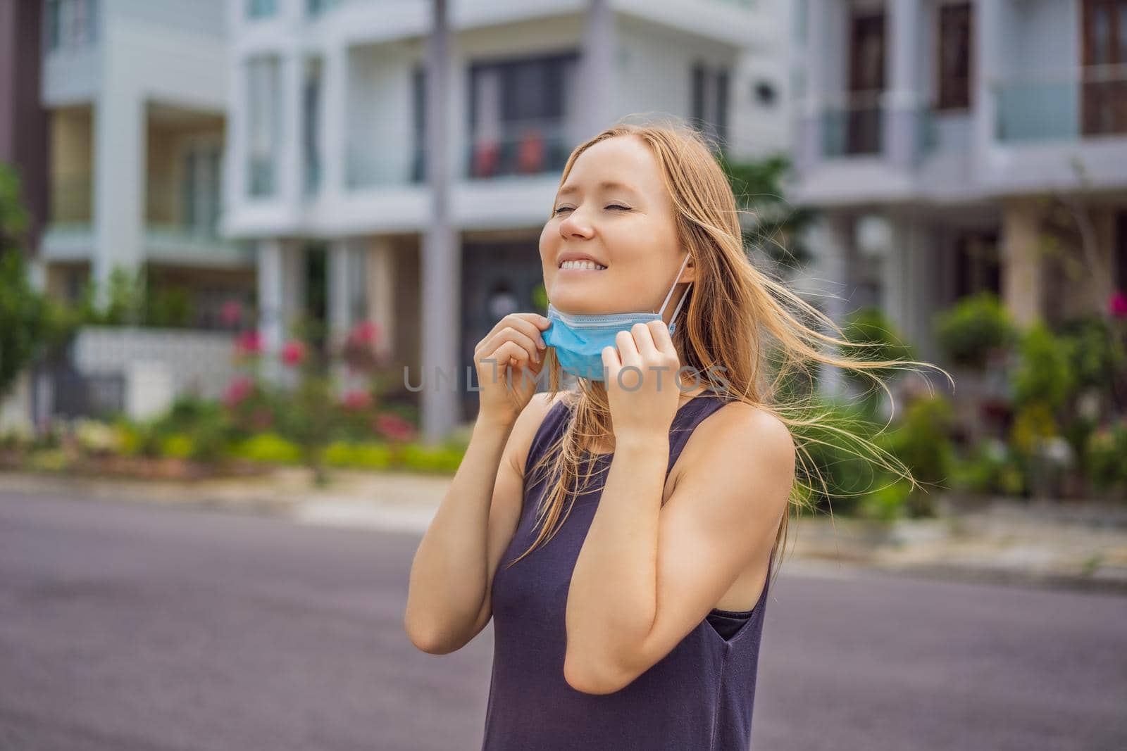 Quarantine is over concept. Woman taking off mask against the background of small town houses. We are safe. Coronavirus ended. We won. No more quarantine. Breathe deep. Take off the mask. Coronavirus is over.