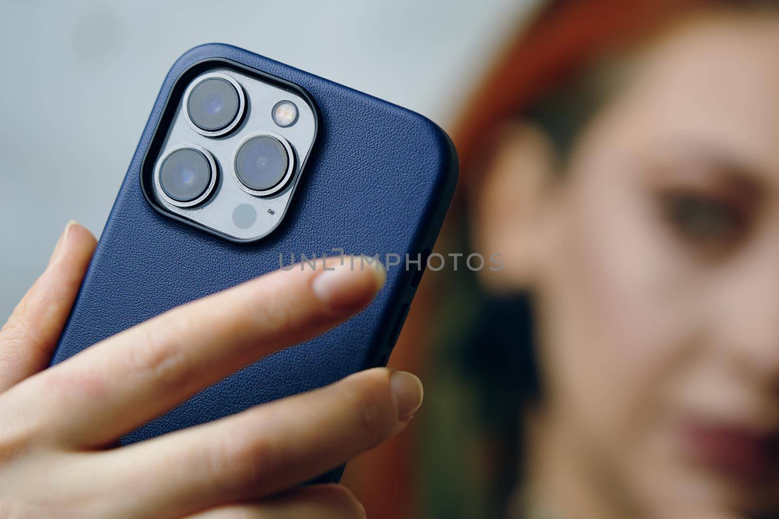 Female blogger takes selfie on iPhone 13 pro. Gadget with triple-lens camera. Close-up of woman's hand holding smartphone in case. Focus on foreground. Bishkek, Kyrgyzstan - January 24, 2022