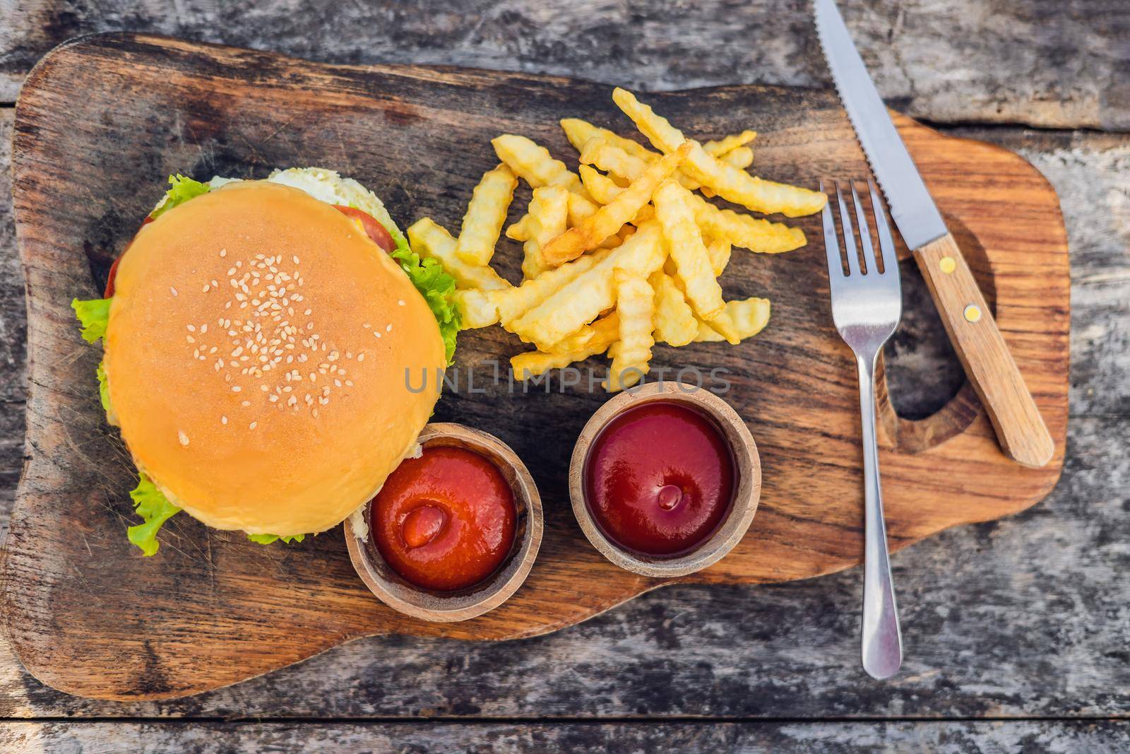 Closeup of fresh burger with French fries on wooden table with bowls of tomato sauce. lifestyle food.