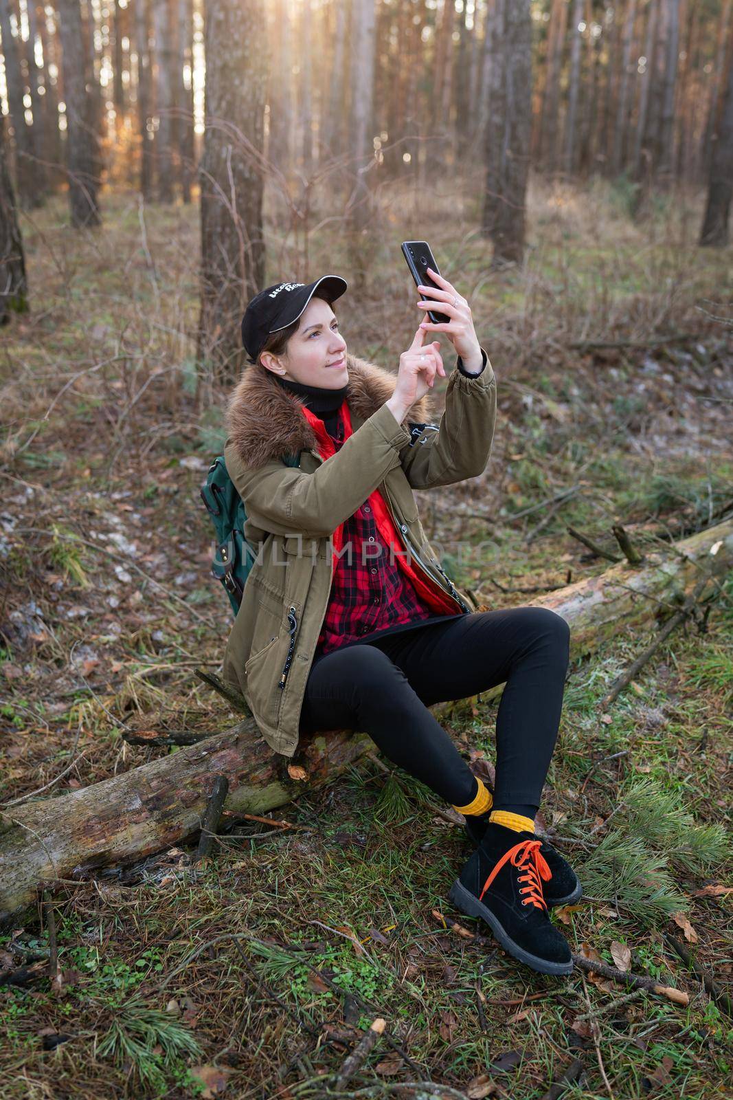 The girl sits on a log in the forest and takes pictures of the beautiful views of the forest. Travel, trekking and hiking