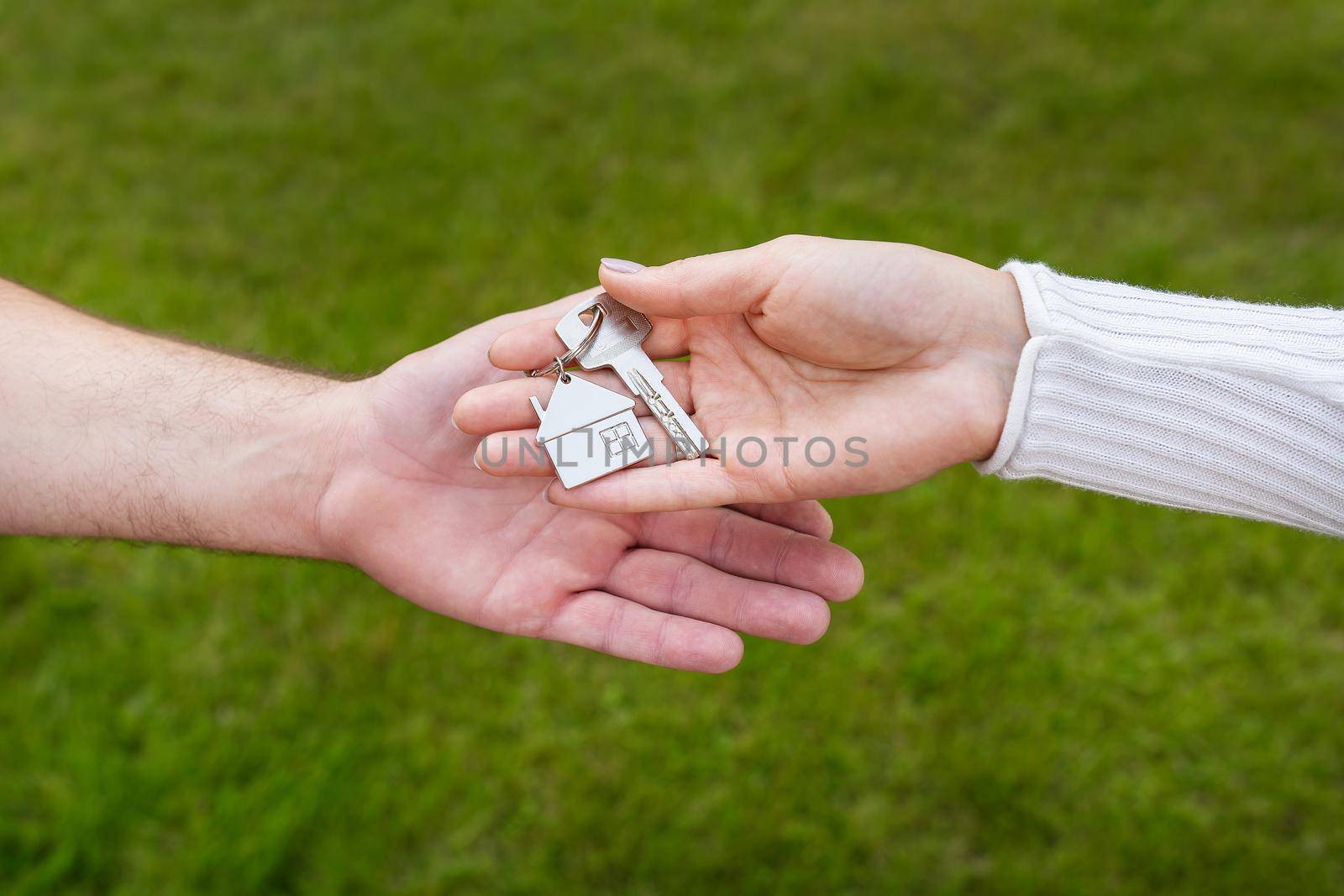 Keys with a keychain in the form of a metal house from a new house or apartment in the hands of a young family. Happiness from buying a house. Handing over the keys from the realtor