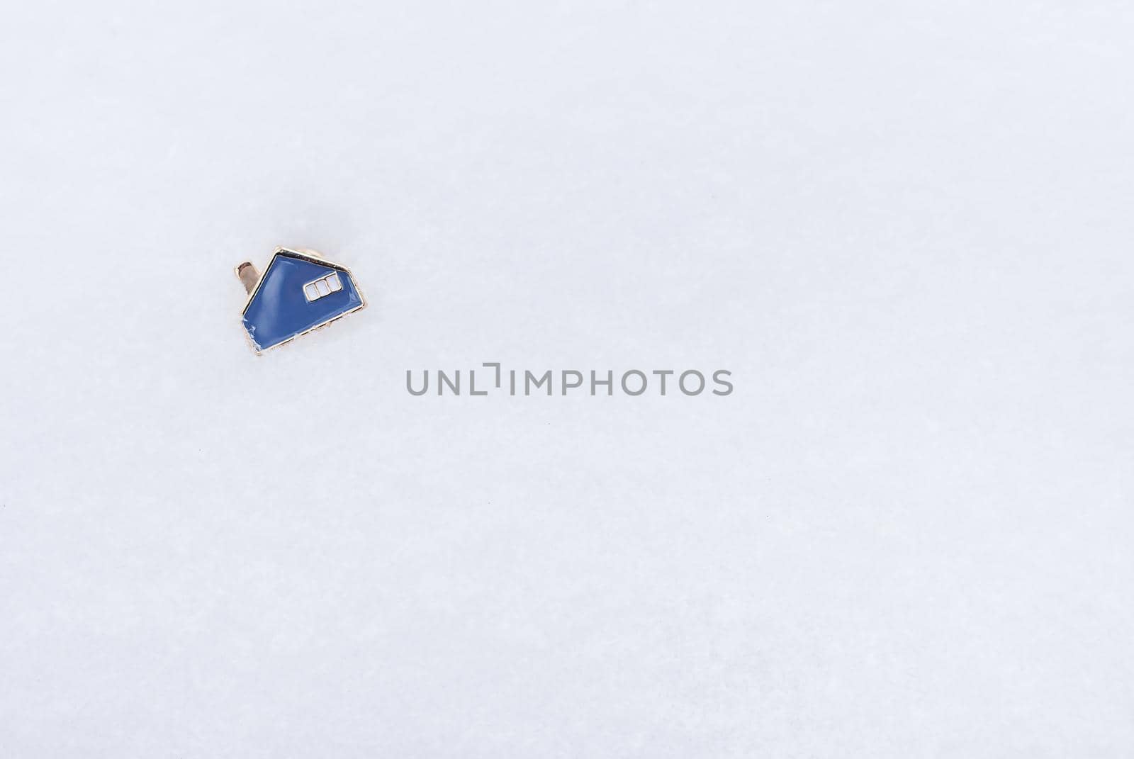 A metal small blue house that lies on the snow. Place for an inscription. Real estate and mortgage concept