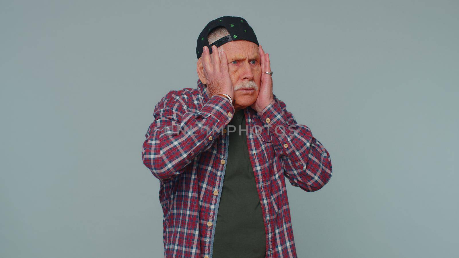Stressed depressed mature man 80 years old in shirt expresses his fear and waves his hands away from danger, waving no. Scared fearful senior grandfather isolated alone on gray studio wall background