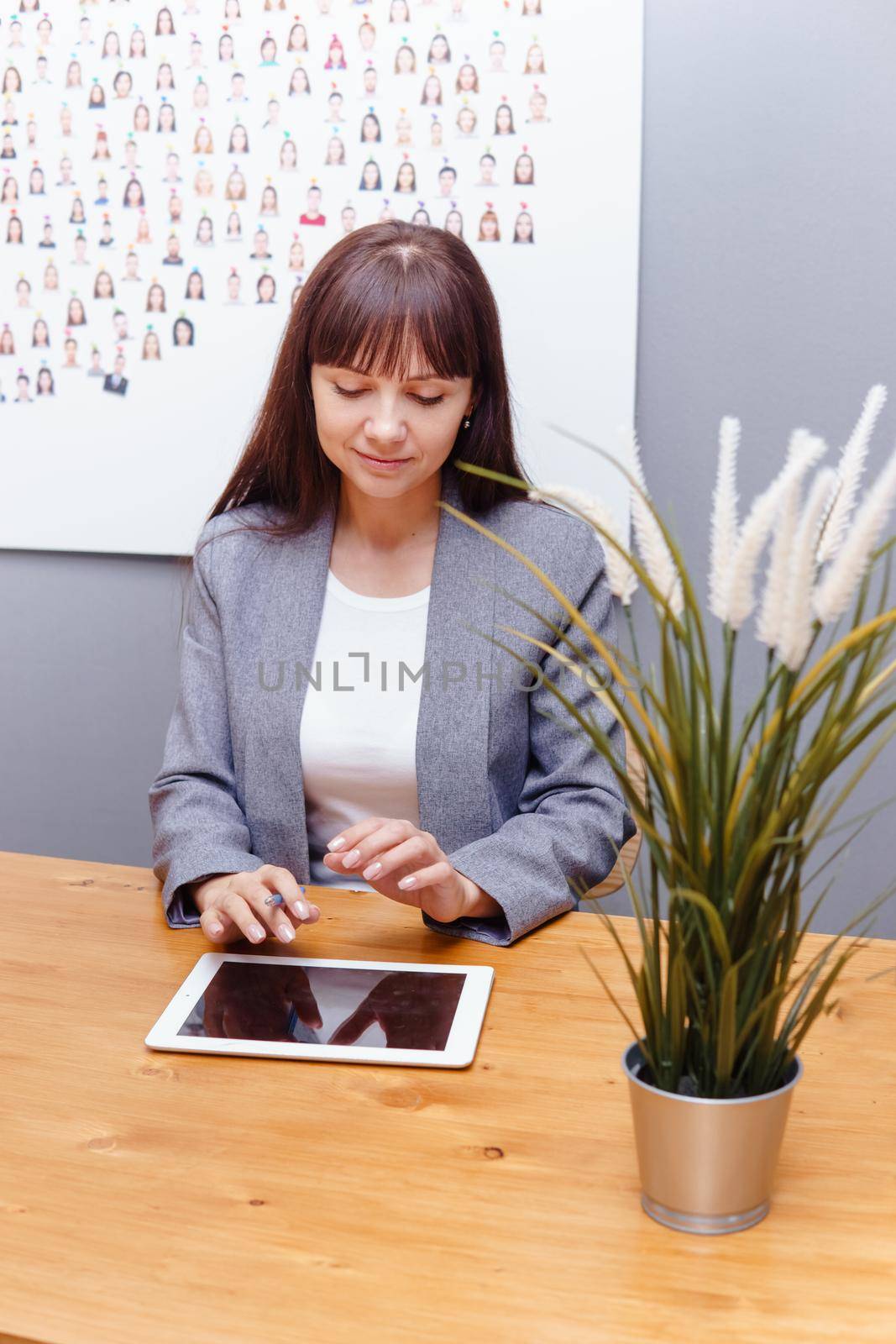 A brunette businesswoman in a gray jacket at her desk with a tablet in her hands. Business portrait in the office.