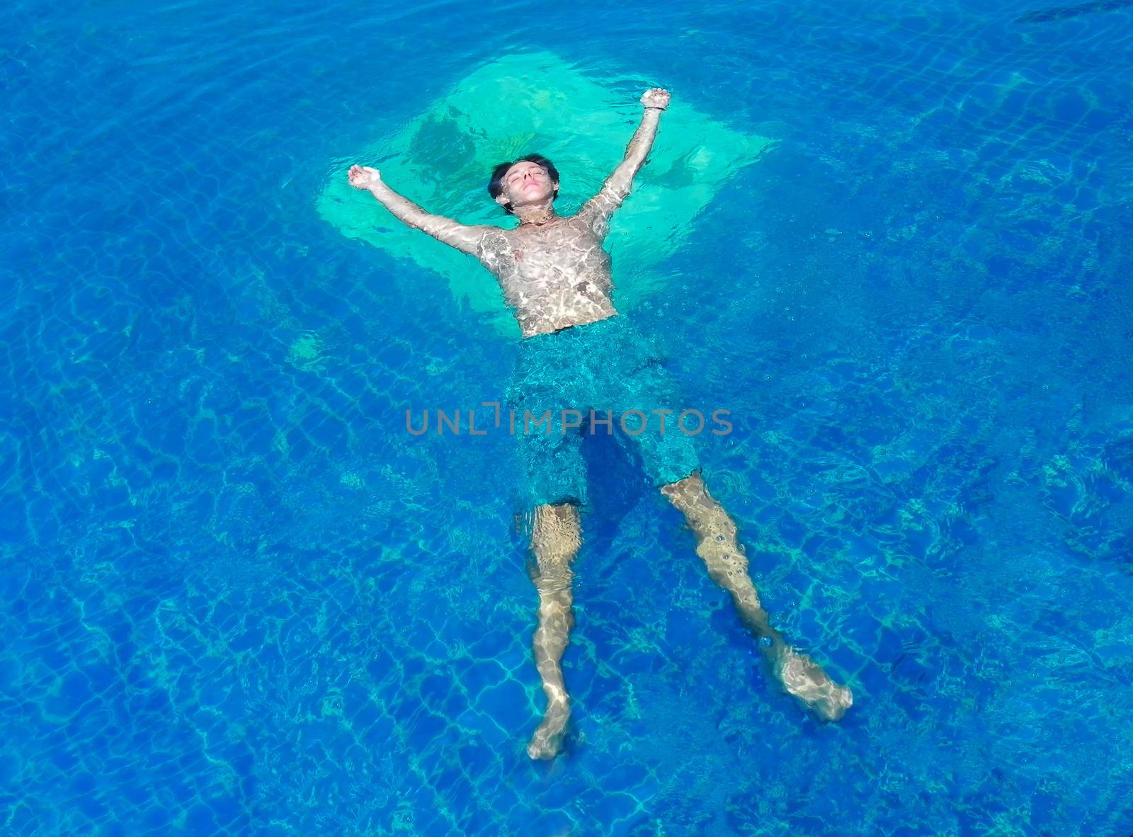 young men in swim short standing on the edge of an infinity pool during vacation in Santorini Greece by Andre1ns