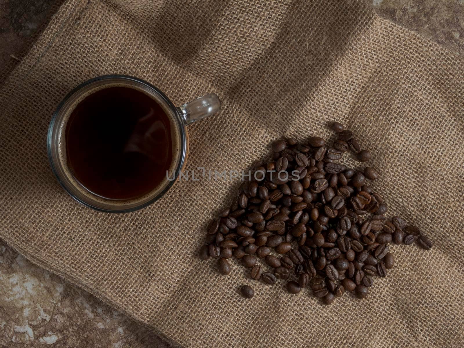 dark roasted coffee beans on burlap and a mug of freshly brewed natural coffee.