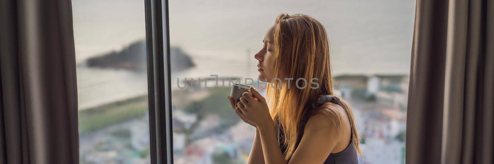 Young woman is drinking coffee in the morning on the background of a window with a sea view BANNER, LONG FORMAT by galitskaya