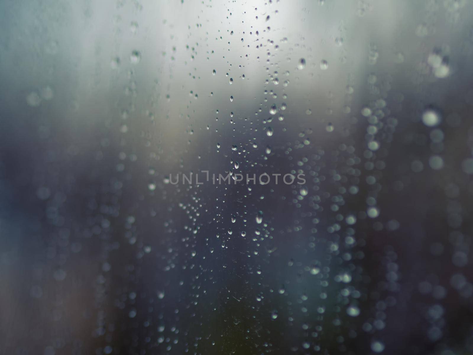 Raindrops on the surface of window glass with a blurred background.