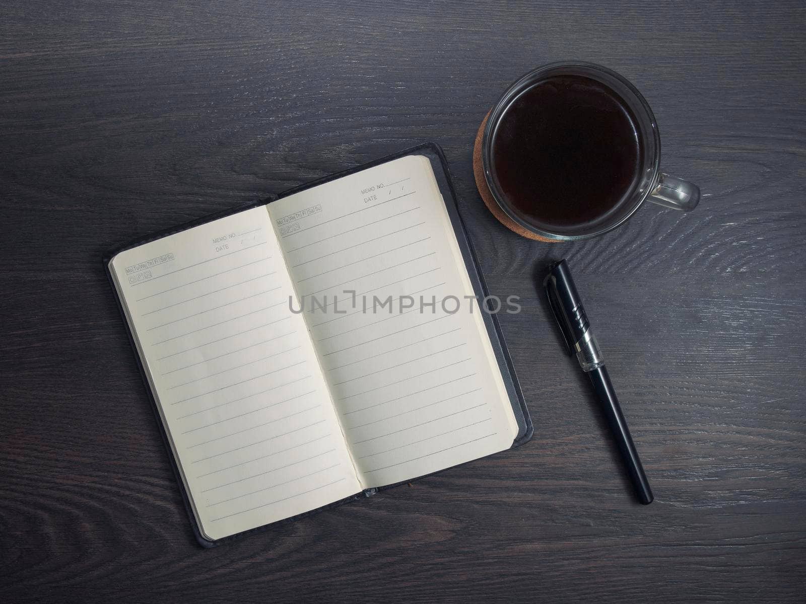 Workplace with notebook, pen and glass coffee mug on wooden background.