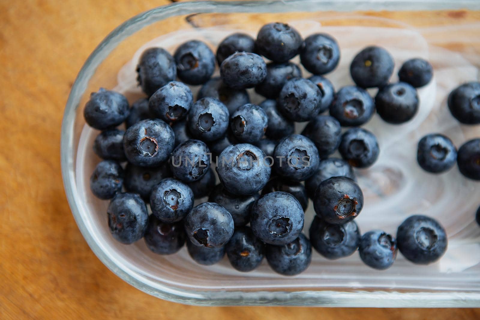 Fresh blueberries in a transparent plate on a wooden table. Top view, natural vitamins