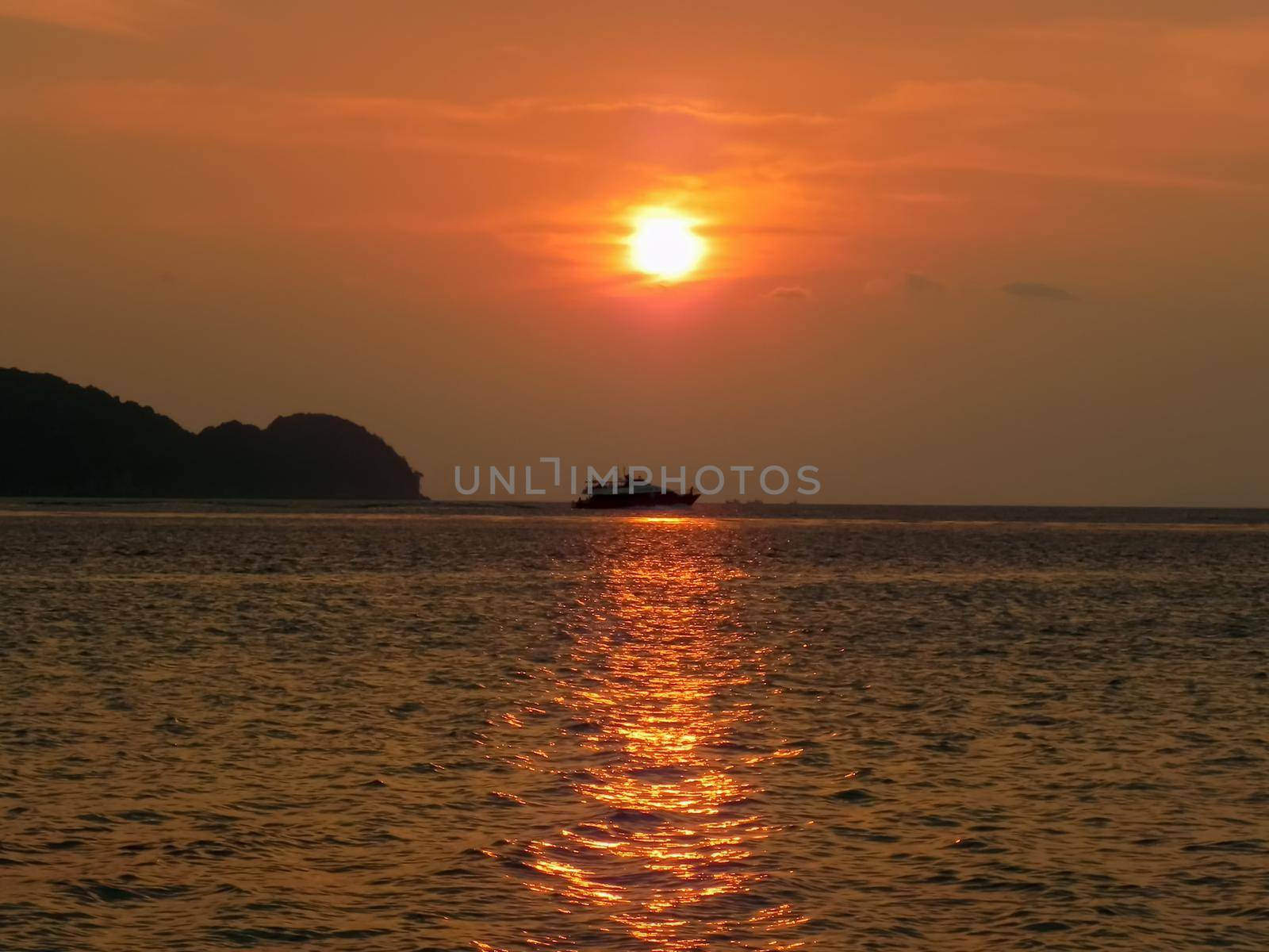 Fishing boat at sea on the horizon during sunset.