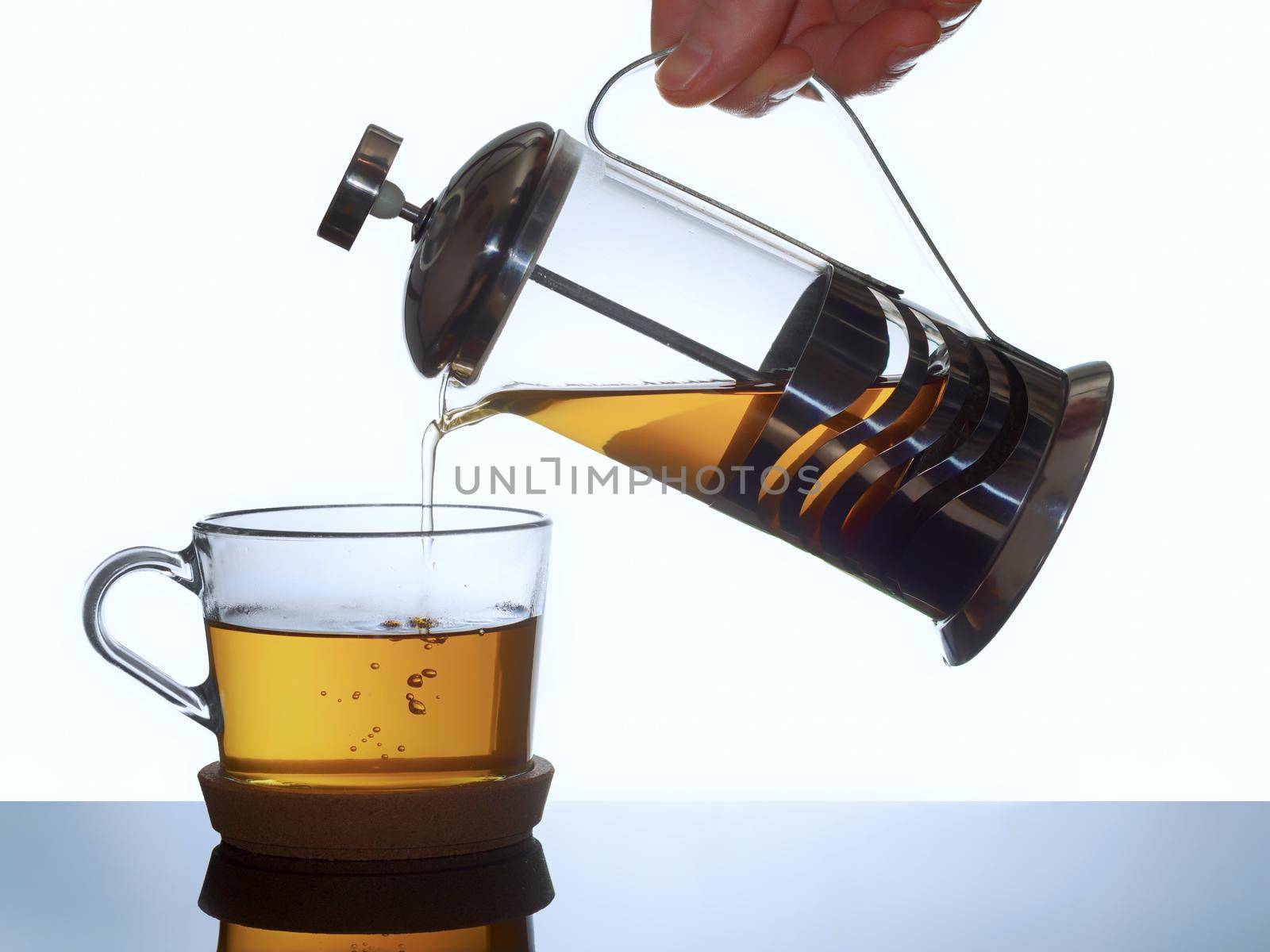 Transparent glass mug and french press with warm tea on a light background.