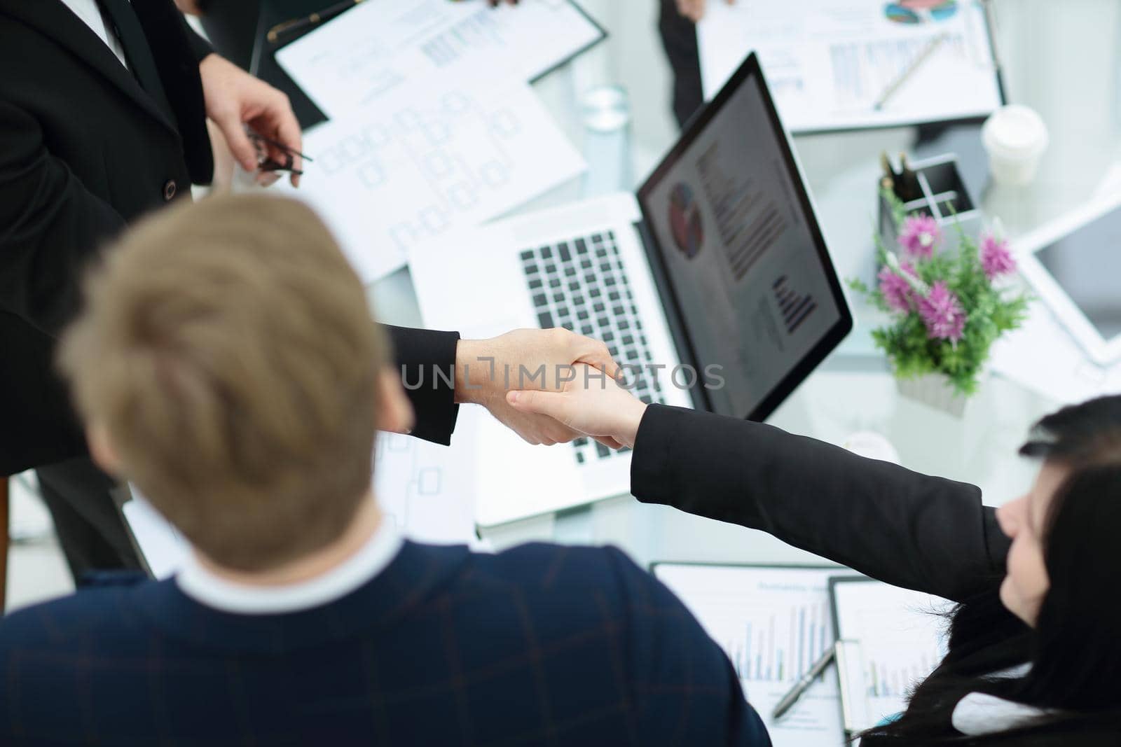 Young smiling businessman and businesswoman shaking hands over the table on meeting by SmartPhotoLab