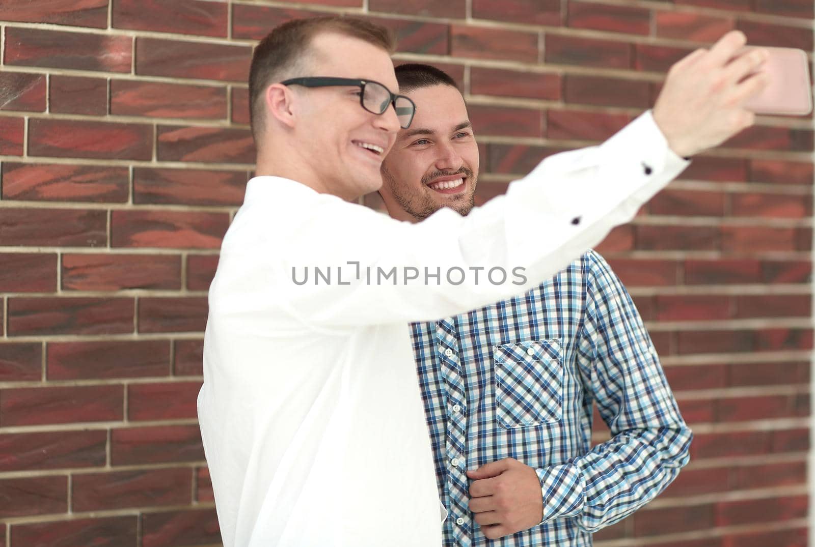 two young men taking selfies standing near a brick wall .people and technology