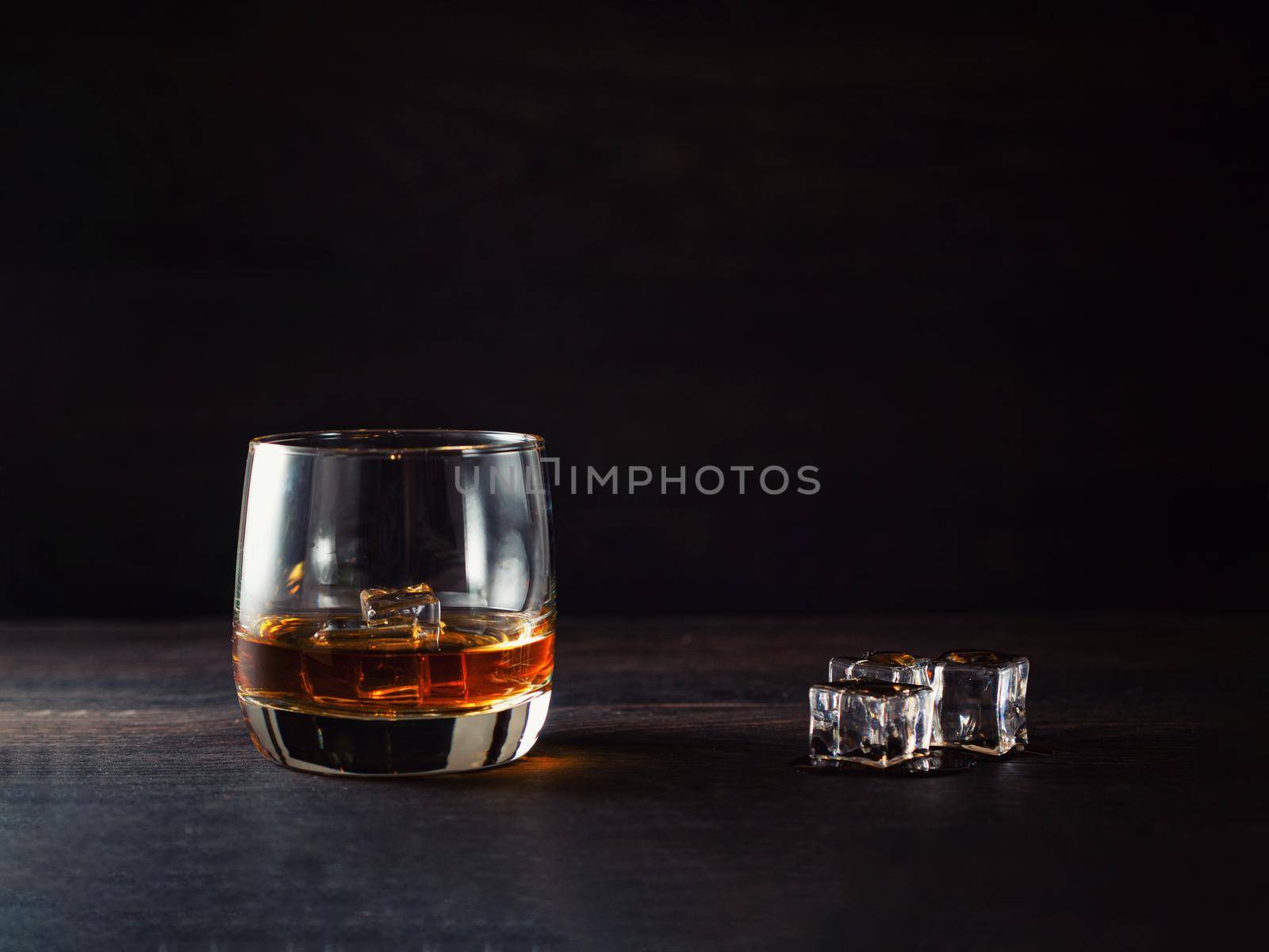 Whiskey splash in a glass with ice on a wooden table.