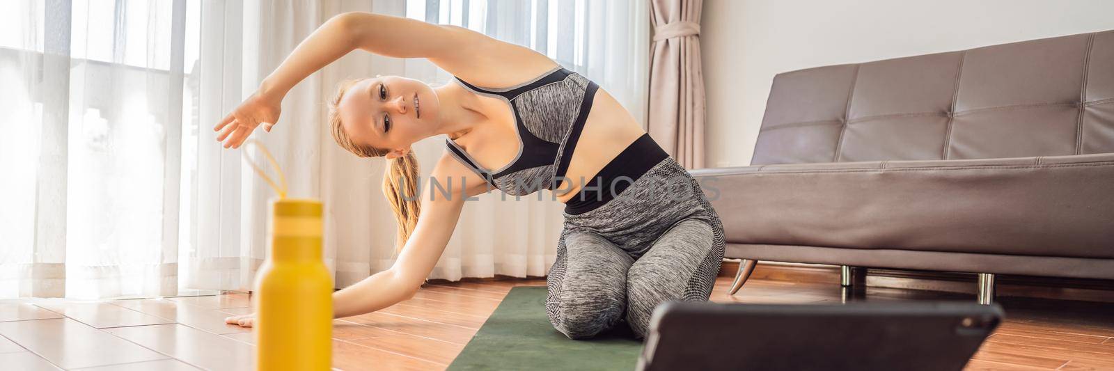 Fitness woman exercising on the floor at home and watching fitness videos in a tablet. People do sports online because of the coronovirus. BANNER, LONG FORMAT