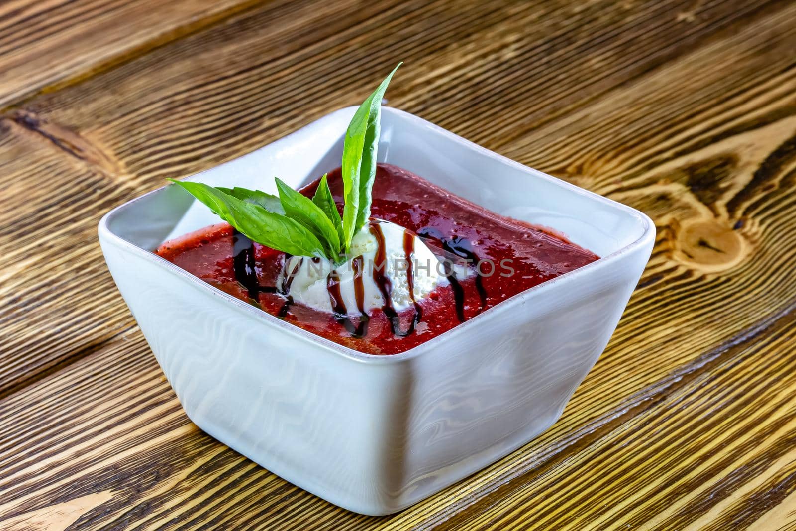 Tasty sweet dessert of ice cream poured with berry sirup in glass ramekin on wooden table. From above. Unfocused background.