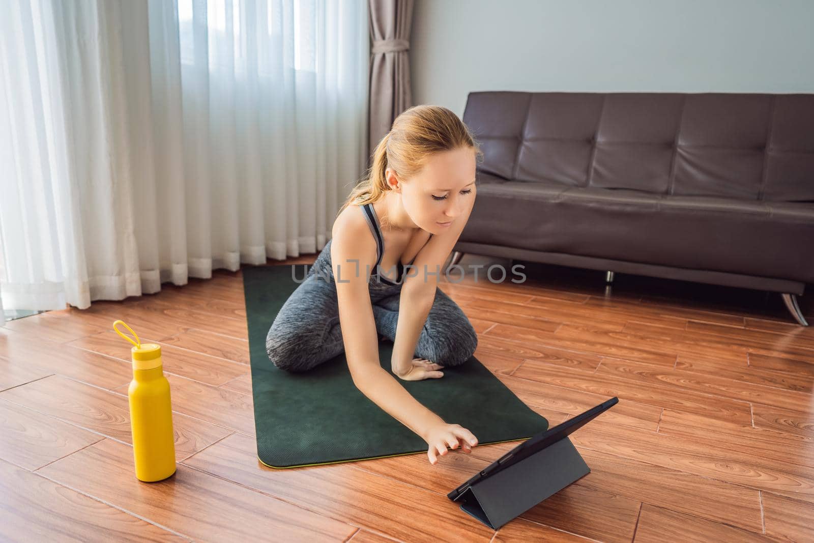 Fitness woman exercising on the floor at home and watching fitness videos in a tablet. People do sports online because of the coronovirus by galitskaya