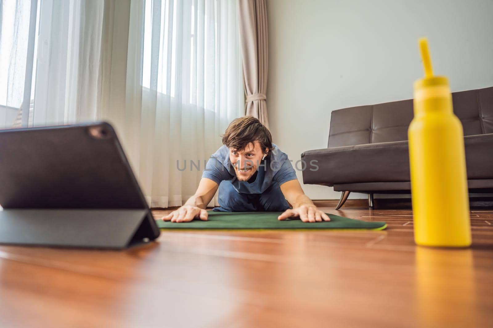 Fitness man exercising on the floor at home and watching fitness videos in a tablet. People do sports online because of the coronovirus by galitskaya