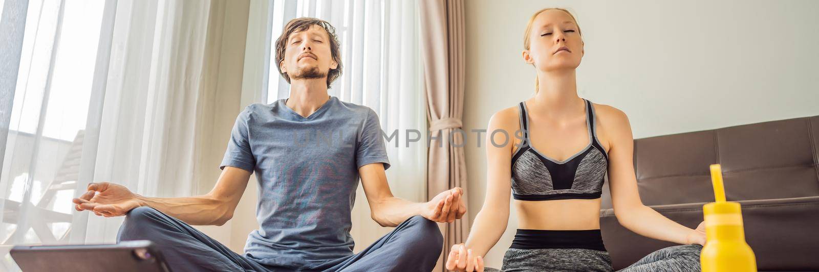 Fitness man and woman exercising on the floor at home and watching fitness videos in a tablet. People do sports online because of the coronovirus. BANNER, LONG FORMAT
