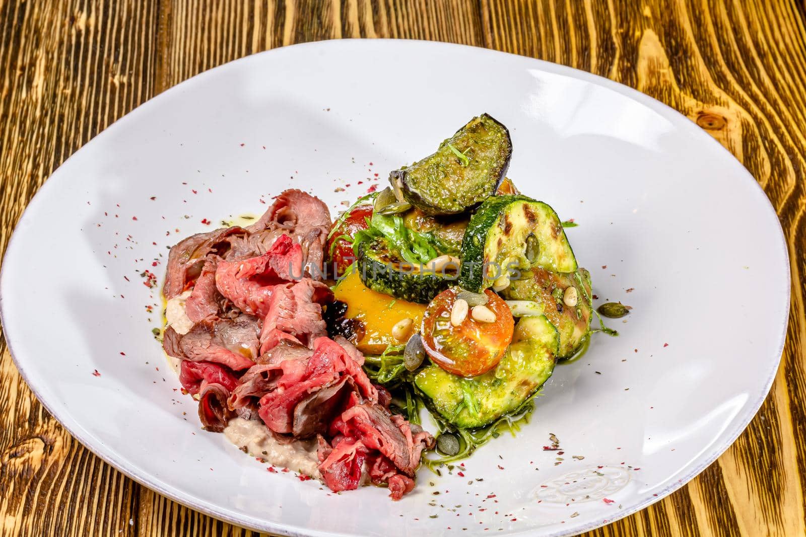 Sliced rare roast sirloin of beef with roasted vegetables on rustic wooden background.