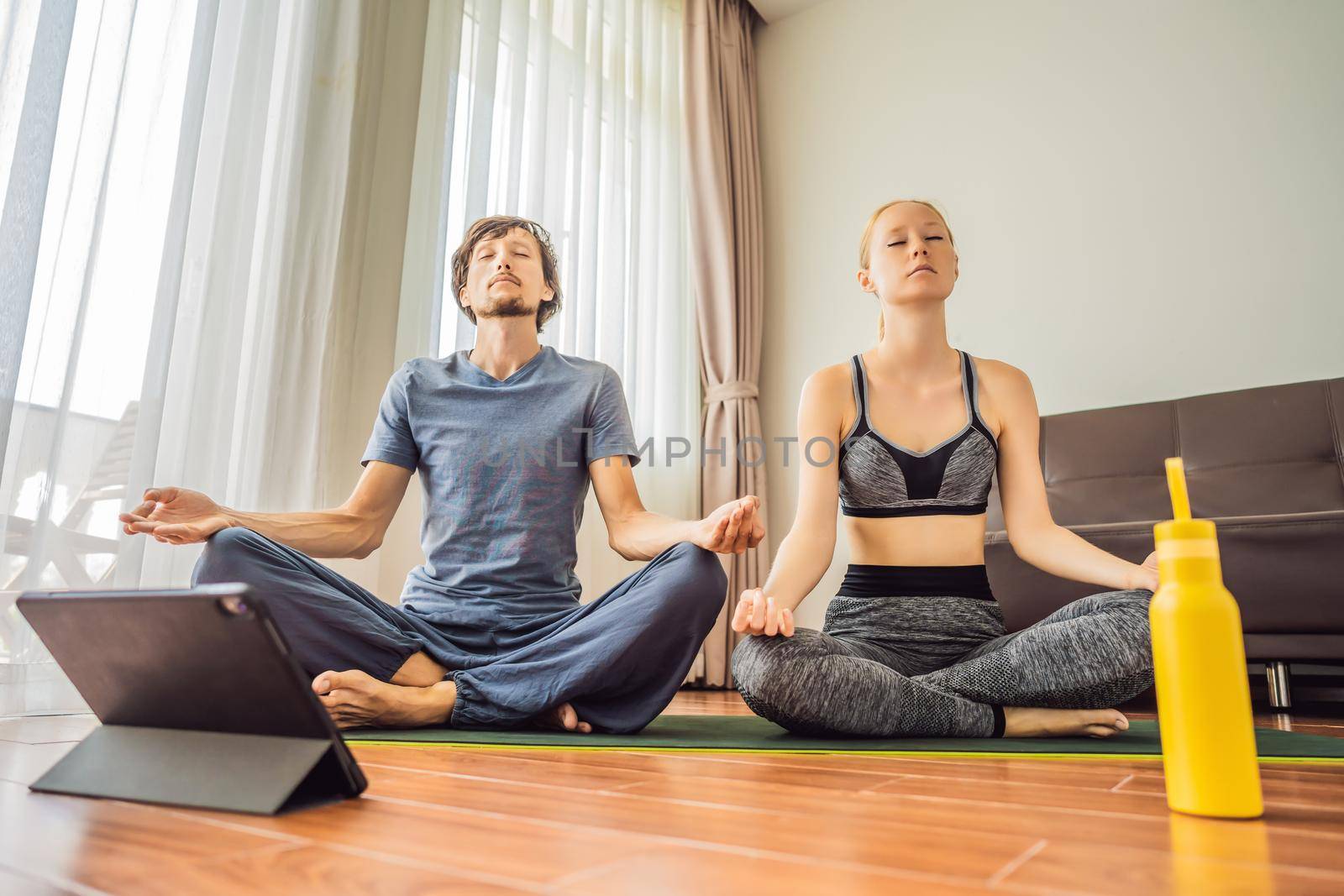 Fitness man and woman exercising on the floor at home and watching fitness videos in a tablet. People do sports online because of the coronovirus.