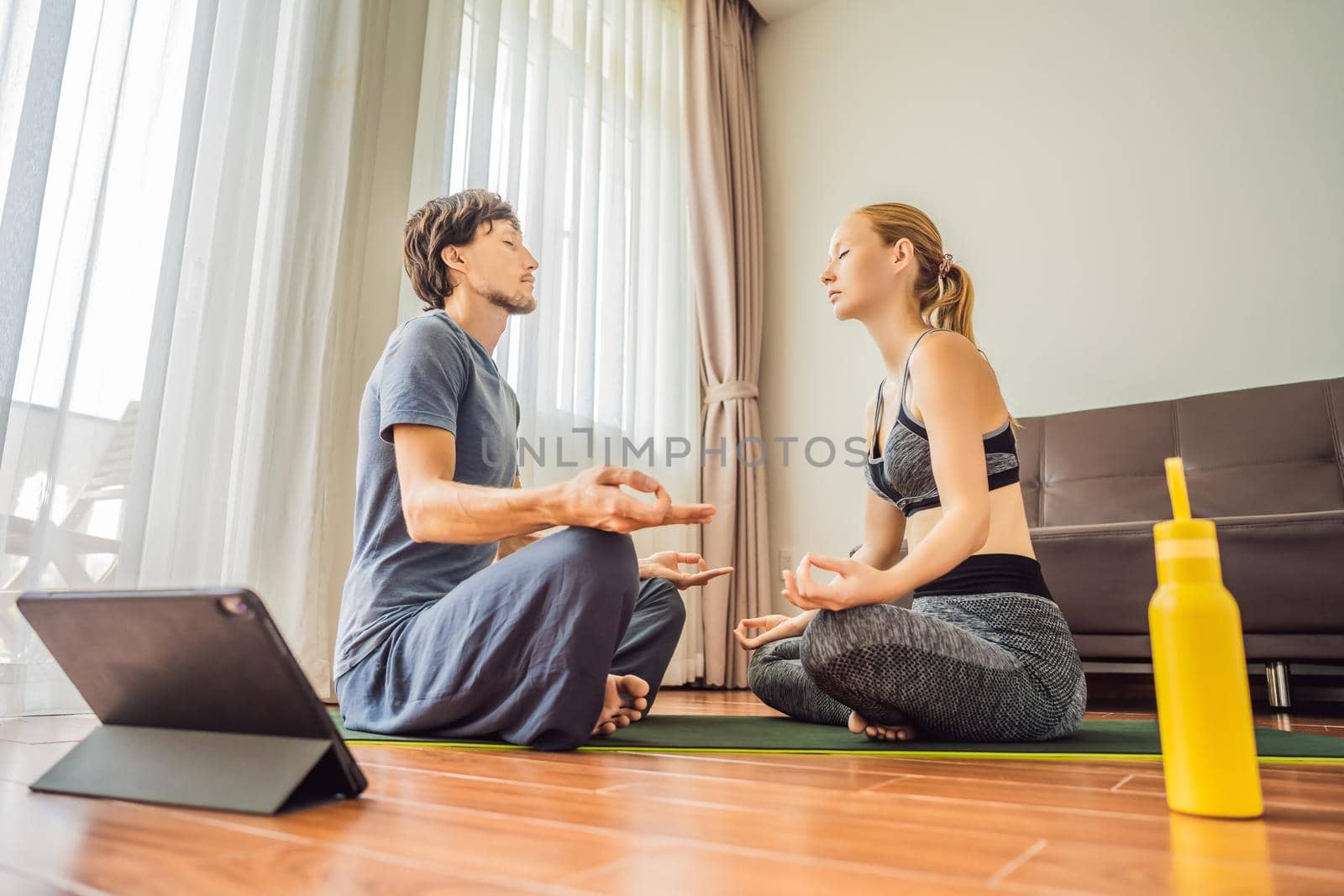 Fitness man and woman exercising on the floor at home and watching fitness videos in a tablet. People do sports online because of the coronovirus by galitskaya