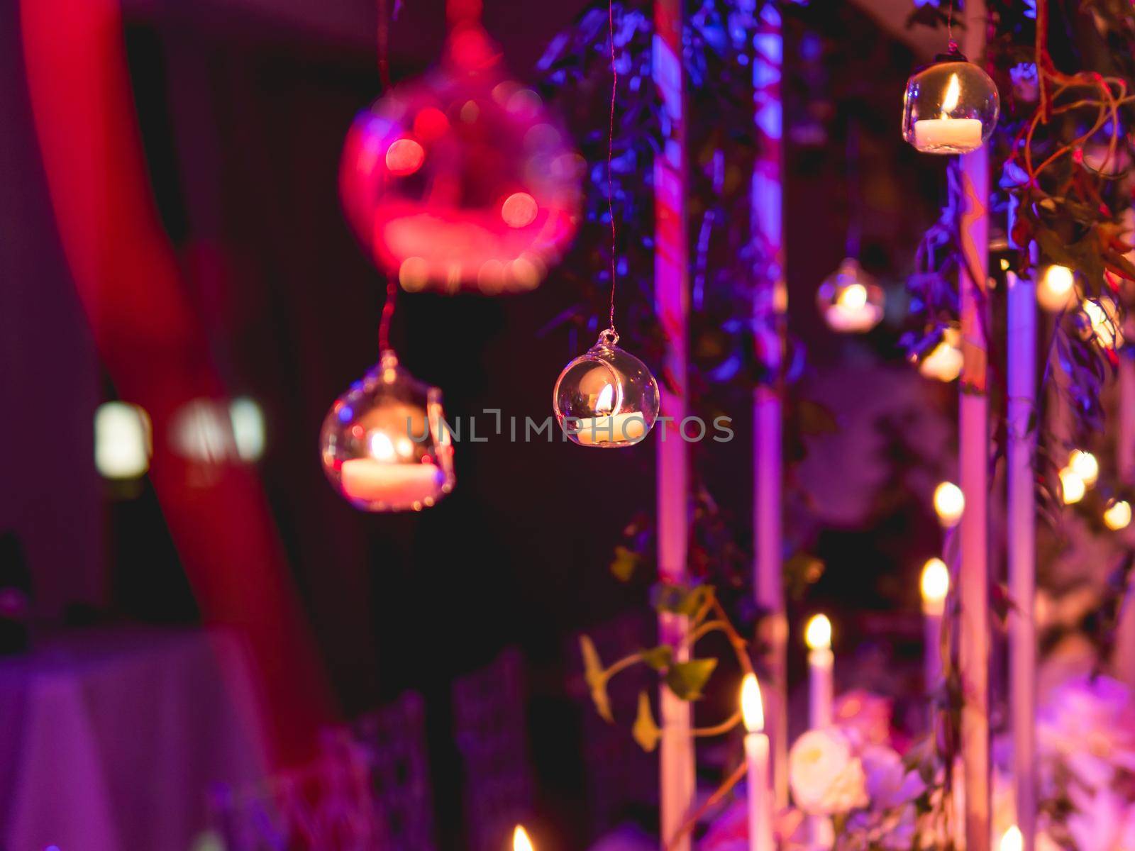 Candles in small glass circlular candle holders handled on strings. Beautiful decorations in purple electric light. by aksenovko