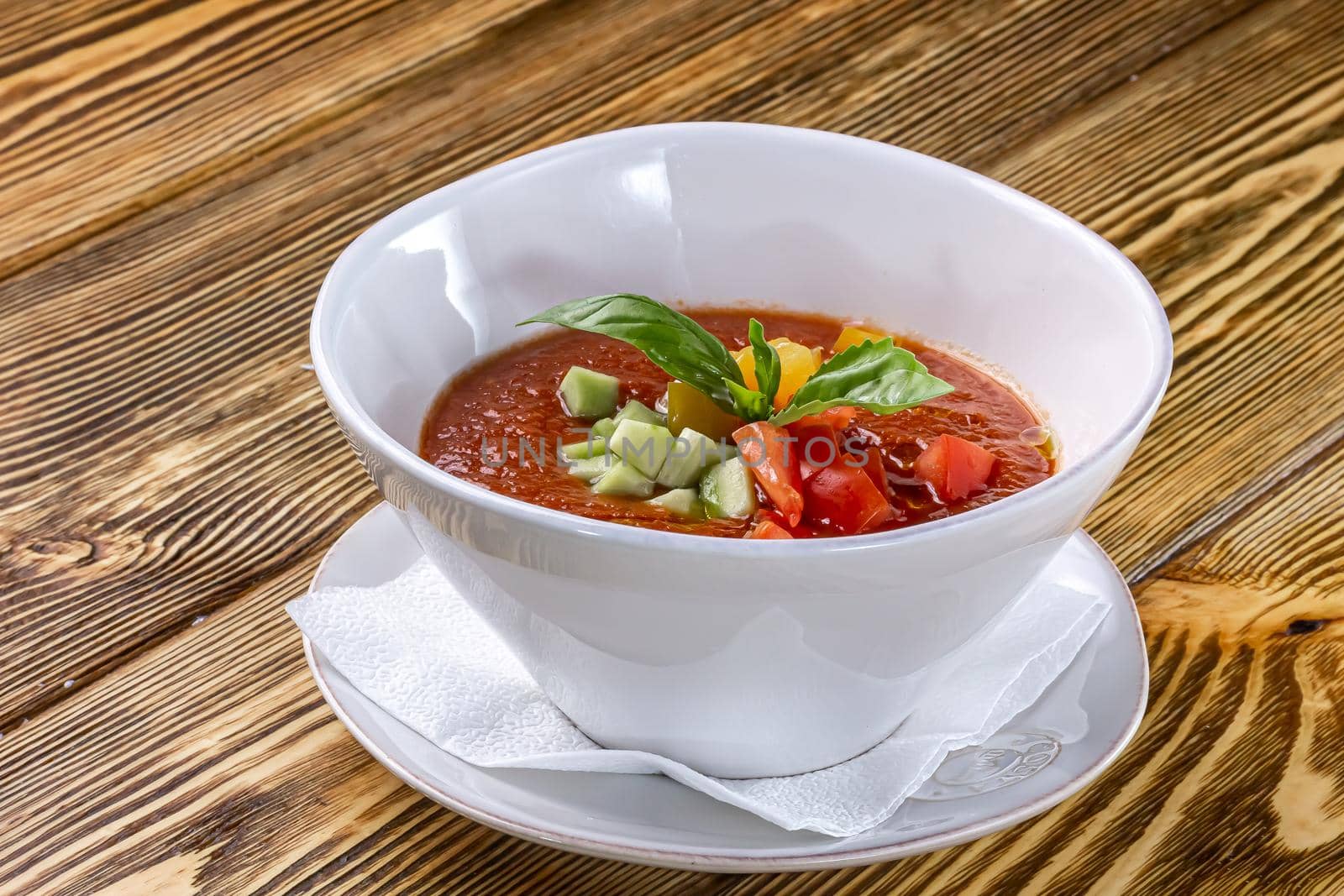 Raw tomato soup, typical food of Spain, served in white bowls with pieces of tomato, cucumber and paprika. Wooden background.
