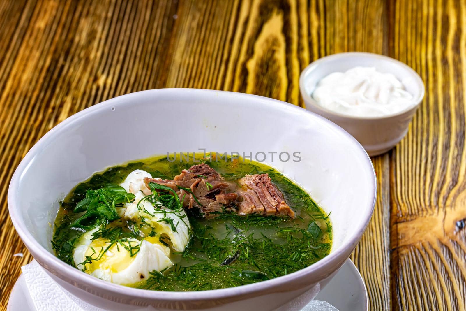 Green Sorrel soup with with boiled eggs wedges in white bowl. Selective focus, bunch of fresh sorrel on background.