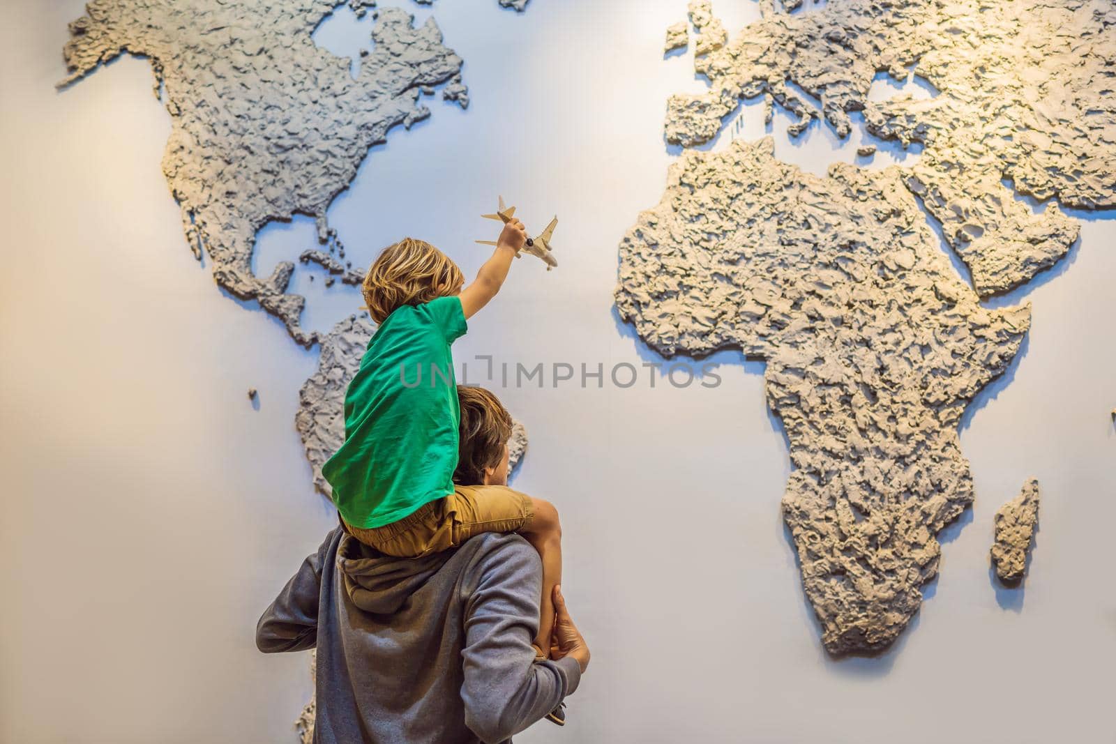 Coronavirus is over. Quarantine weakened. Take off the mask. Now you can travel. Dad and son on the background of a world map with an airplane in his hands. Travel concept.