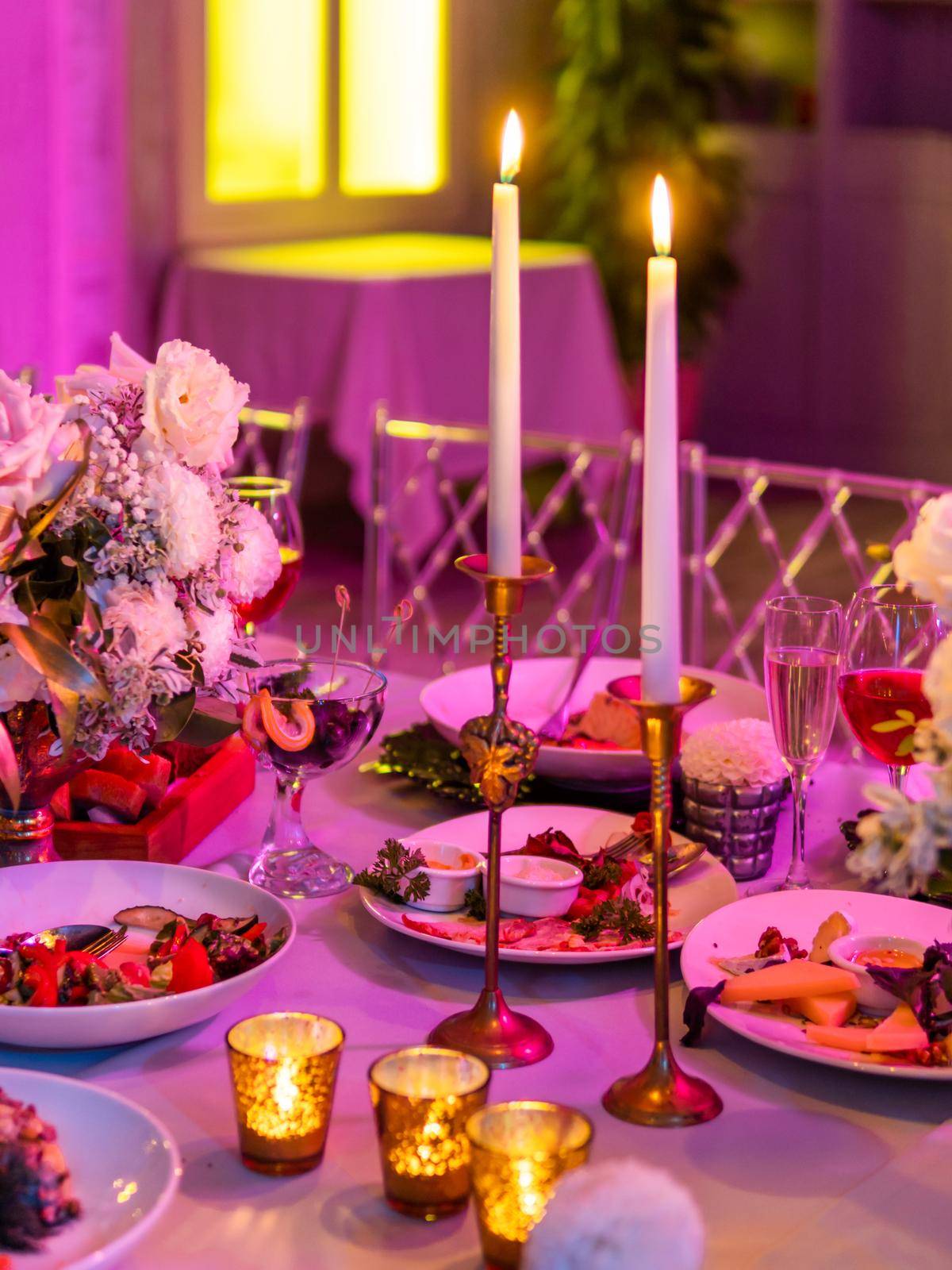 Table served for banquet or romantic date with candles and floral compositions. Beautiful decorations in pink electric light. by aksenovko