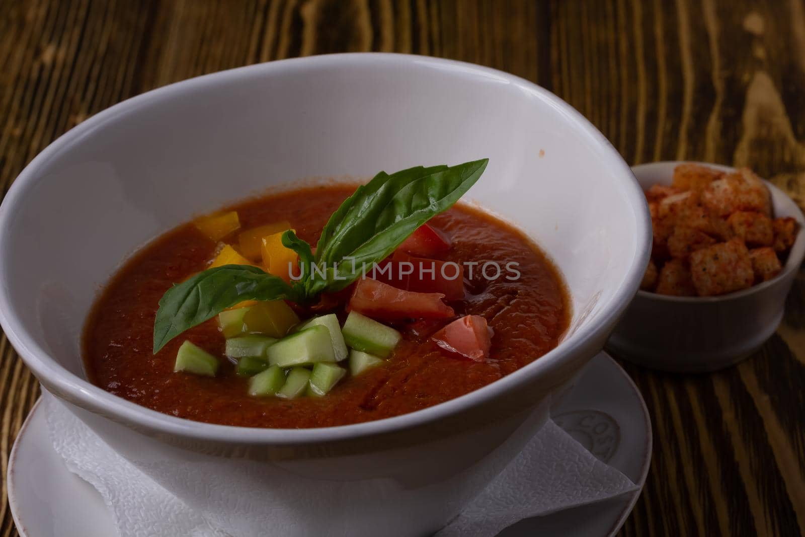 Raw tomato soup, typical food of Spain, served in white bowls with pieces of tomato, cucumber and paprika. Wooden background by Milanchikov