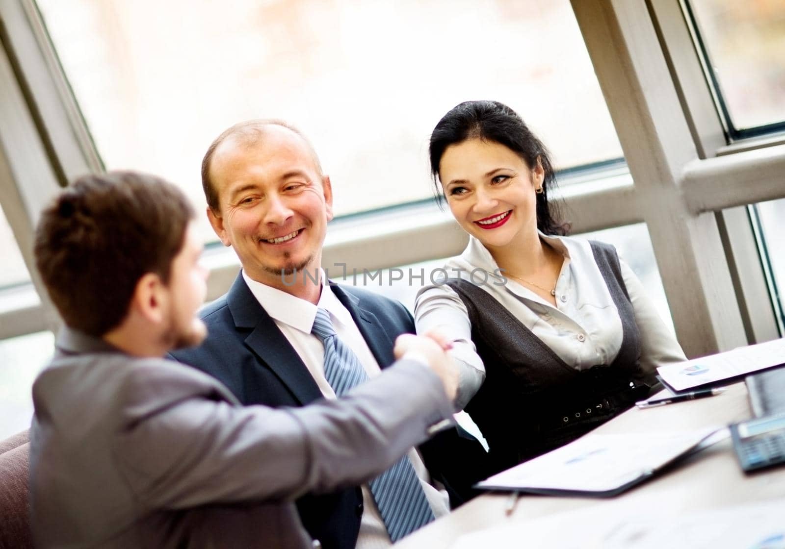 Mature businessman shaking hands to seal a deal with his partner and colleagues in a modern office