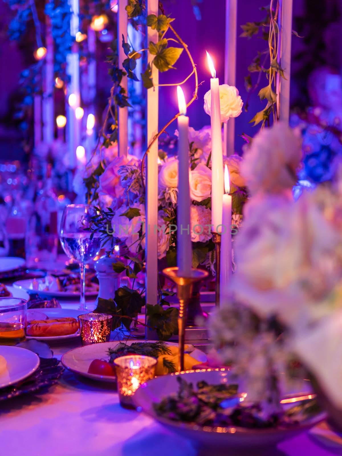 Table served for banquet with candles and floral compositions. Beautiful decorations in blue and purple electric light. by aksenovko