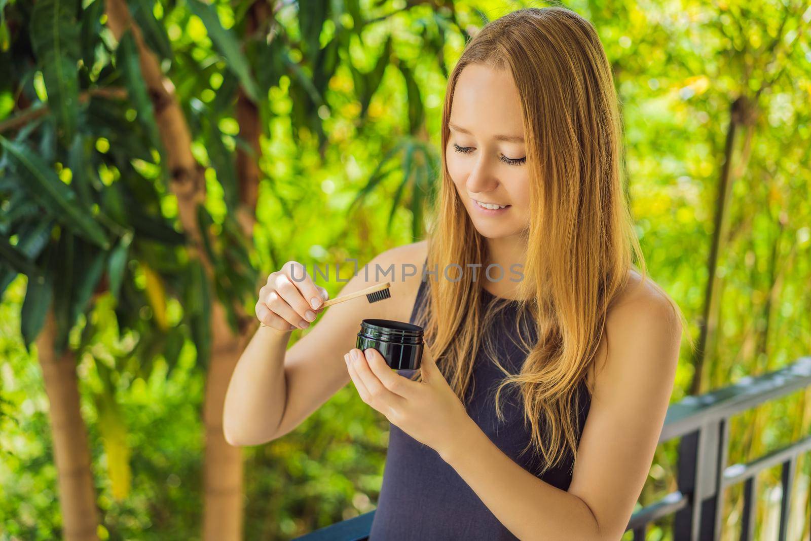 Young woman brush teeth using Activated charcoal powder for brushing and whitening teeth. Bamboo eco brush.