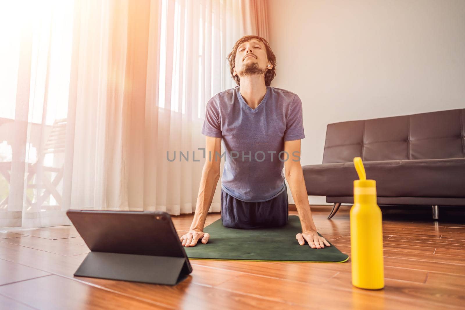 Fitness man exercising on the floor at home and watching fitness videos in a tablet. People do sports online because of the coronovirus by galitskaya