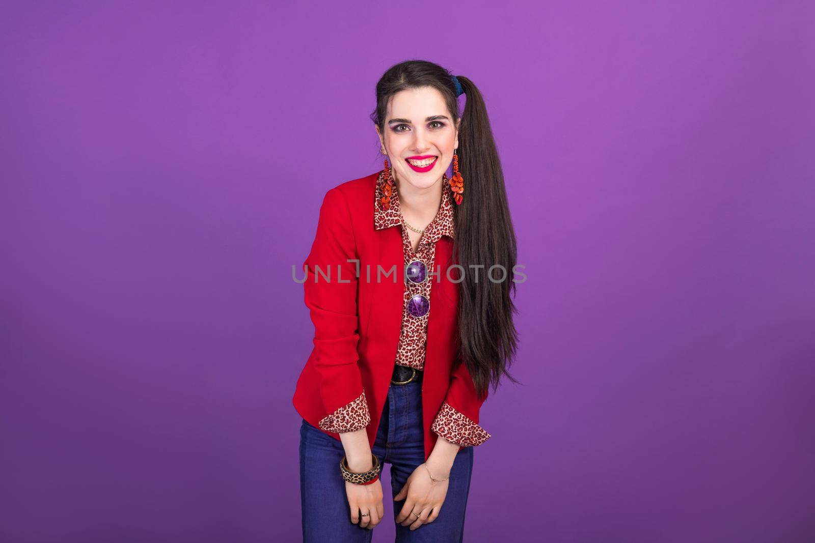 Happy laughing young brunette woman in 90s style in red jacket on purple background.