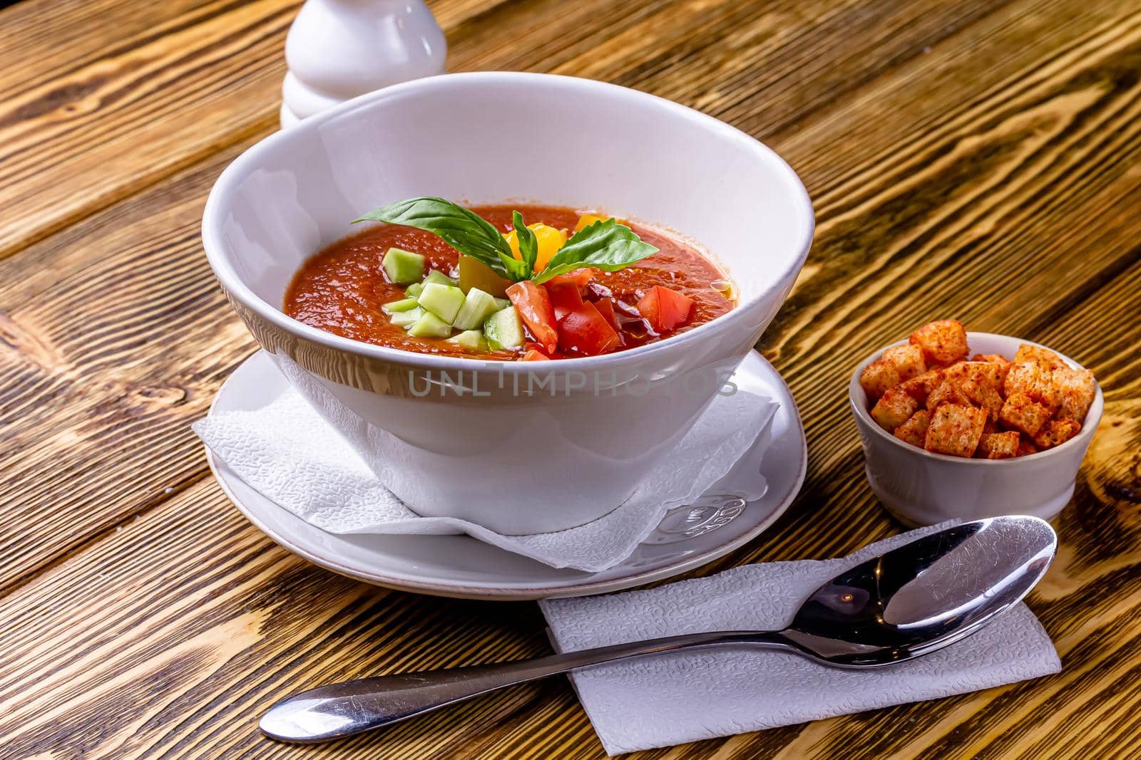 Raw tomato soup, typical food of Spain, served in white bowls with pieces of tomato, cucumber and paprika. Wooden background by Milanchikov