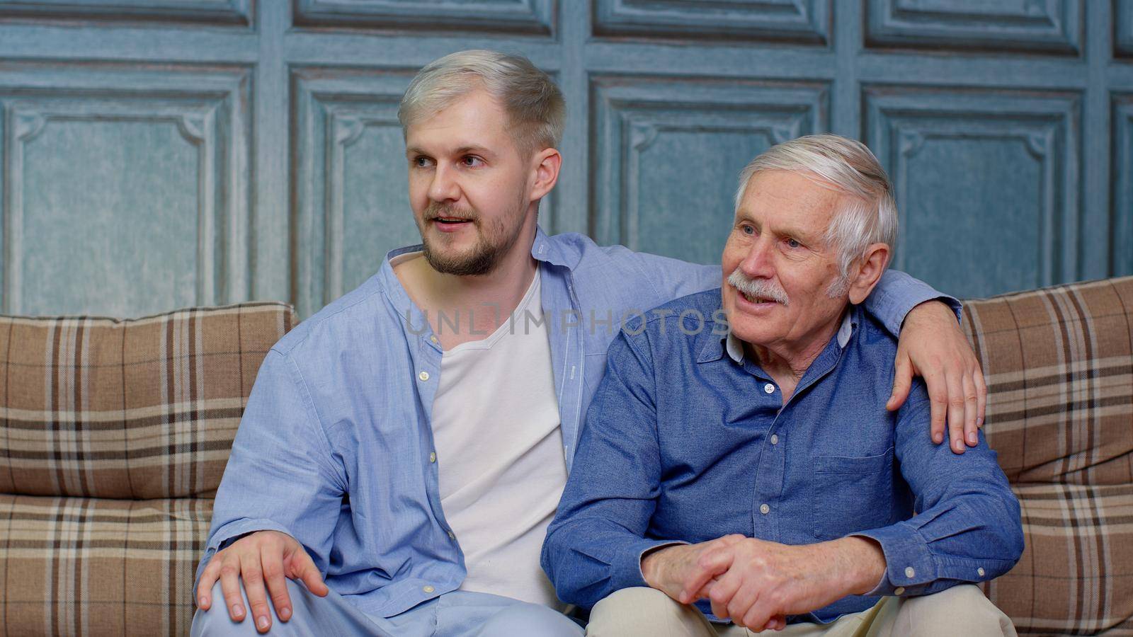 Friendly honest old father and adult son or grandson talking on sofa, happy two generations male family having trust conversation chatting relaxing on couch in room enjoy understanding and support