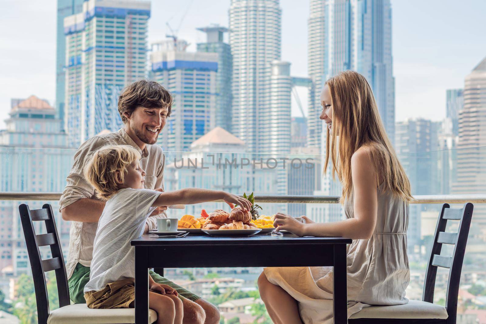Coronavirus is over. Quarantine weakened. Take off the mask. Now you can go to public places. Happy family having breakfast on the balcony. Breakfast table with coffee fruit and bread croisant on a balcony against the backdrop of the big city by galitskaya