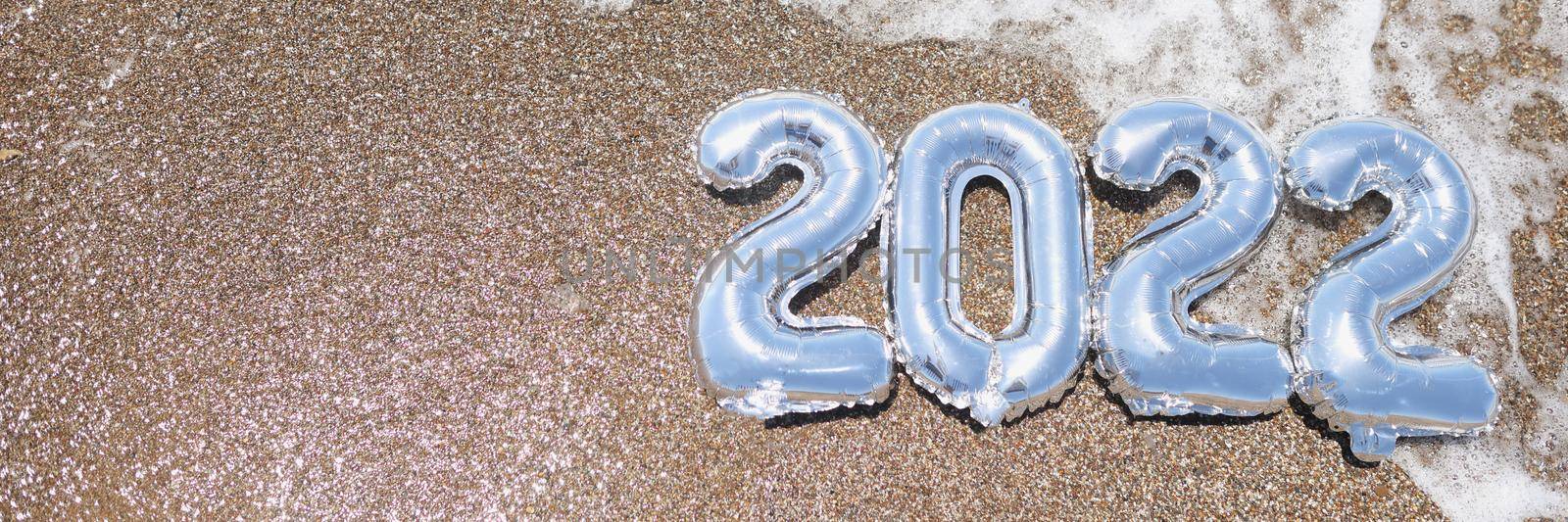 Top view of foil numbers on wet sand and foam wave on beach. Copy space in left. Waiting for the new year and new life, meet new year on holiday. Christmas, new year concept