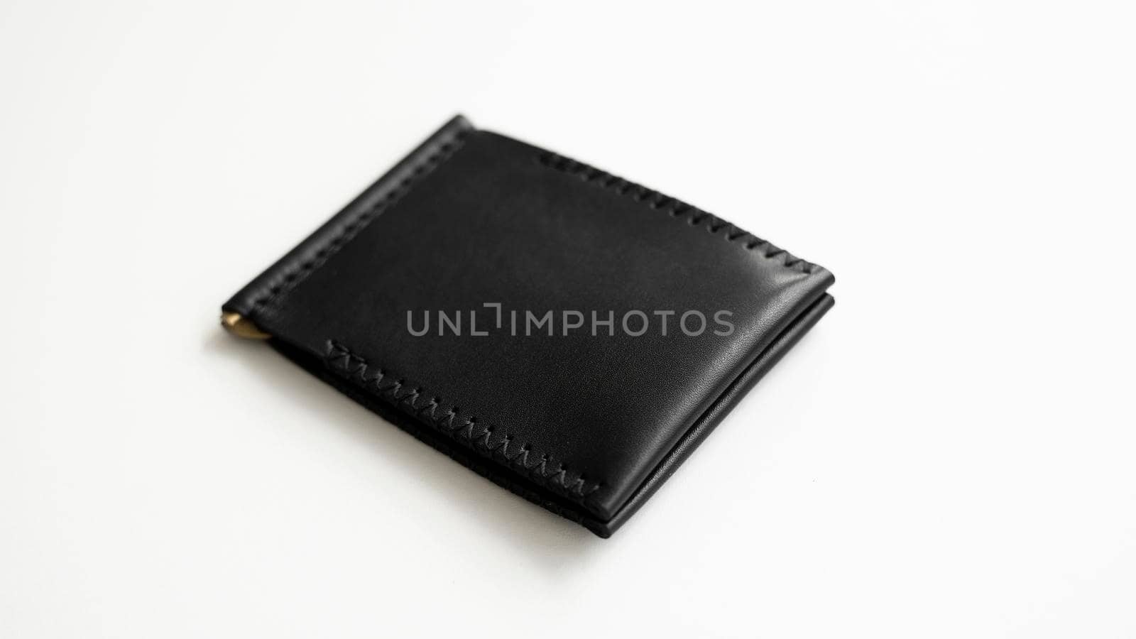 Empty black men's money clip handmade leather wallet with a two pockets for cards lies on a white table. Selective focus, copy space, close up